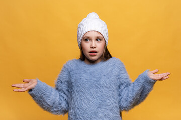 Puzzled and clueless little girl with arms out, shrugging her shoulders, on yellow background, saying: who cares, so what, I don't know. Negative human emotions, facial expressions, life attitude