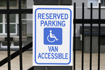 Reserved parking sign for disabled drivers. Accessible van parking notice. Blue white wheelchair symbol sign. Urban parking regulation signage. Public accessibility concept.