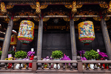 Taipei City, Taiwan - 11 April 2025: View of Longshan Temple's vibrant lanterns casting a warm glow against the dark wood, framed by intricate carvings and lush floral arrangements.