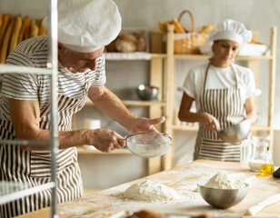 Elderly man and woman sift flour and whipping dough
