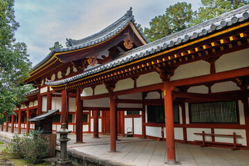 Fototapeta premium Serene Japanese Temple Corridor With Red Wooden Columns, Traditional Rooflines, And Lush Surroundings. Nara City, Japan