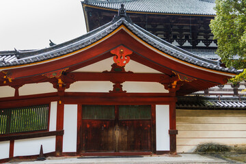 Fototapeta premium Serene Japanese Temple Corridor With Red Wooden Columns, Traditional Rooflines, And Lush Surroundings. Nara City, Japan