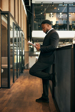 Full length of focused male business expert reading document while standing in office corridor