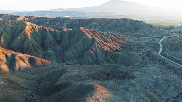 Aerial view of the rugged Calanchi del Cannizzola, its stark ridges and winding paths contrasting with the soft glow of the setting sun, Sicilia, Italy.