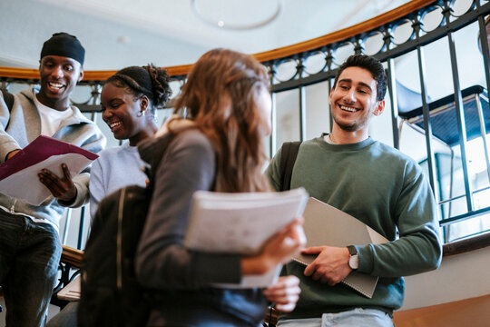 Low angle view of smiling young man talking with female friend while standing on stairs in university building