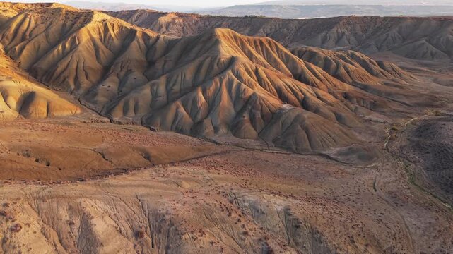Aerial view of the rugged landscape of Calanchi del Cannizzola, where sunlight paints the rolling hills in hues of gold and brown, Centuripe, Sicilia, Italy.