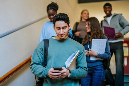 Young male university student using smart phone while moving down on stairs