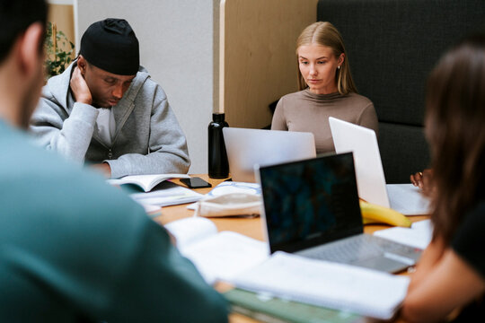 Focused male and female student studying while sitting at table in college campus