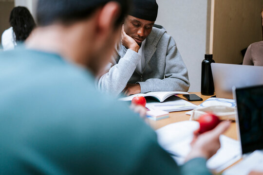 Focused male adult student leaning on elbow while studying in college campus
