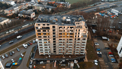 Aerial drone view of modern apartment block under construction beside highway at sunset — residential building site with balconies, flat roof and parking, European urban architecture, no people © Serhii