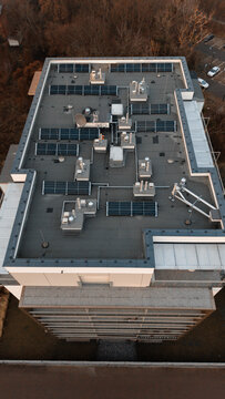 Drone view of modern high-rise rooftop with photovoltaic solar panels, HVAC equipment and antennas on flat roof &mdash; sustainable urban building infrastructure
