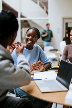 Smiling young woman discussing with male friend while sitting for studies in university campus