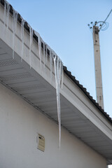 Winter weather conditions concept. Icicle danger in cities concept. Photo of multiple icicles formed on the roof of house. Big sharp dangerous icicles on the roof right over sidewalk.
