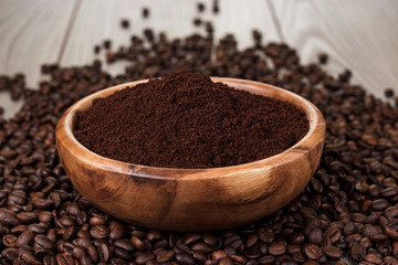 Close up photo of ground coffee in bowl. Wooden bowl full of ground coffee standing on coffee beans scattered over wooden table.