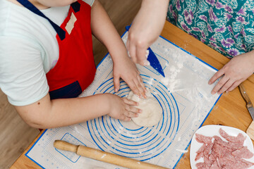 Little boy helping his mother cook for family. Mom and son hand kneading dough for pepperoni pizza. Mother and child cooking homemade pizza together in kitchen.
