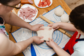 Little boy helping his mother with dinner for family. Mom and child hand kneading dough for homemade pepperoni pizza. Mother and son cooking pizza together in kitchen.