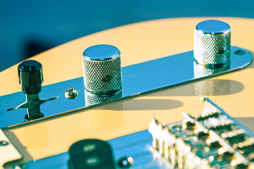 Classic electric guitar control plate showing chrome knobs and black switch against wood body. Metal components reflect blue light, highlighting instrument vintage aesthetic and hardware details