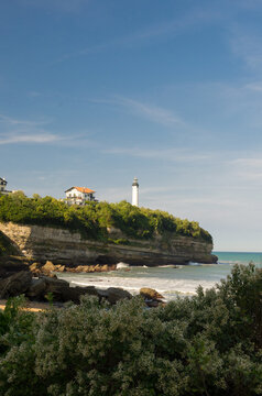 View of a lighthouse standing tall atop a rugged, cliffside perch, overlooking the tranquil, turquoise sea under a clear sky, Anglet, France.
