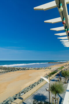 View of the beach with the blue sky and turquoise water meeting the sandy shore under a pergola with colorful lights, Anglet, France.
