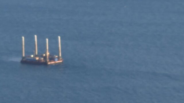 Marine platform, offshore structure, deep blue ocean water, a floating structure with four tall pillars moves across the calm sea, industrial maritime transport