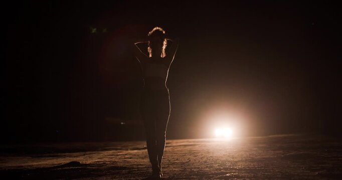 Silhouette of girl walking in front of car headlights on a dark road at night creating a mysterious atmosphere
