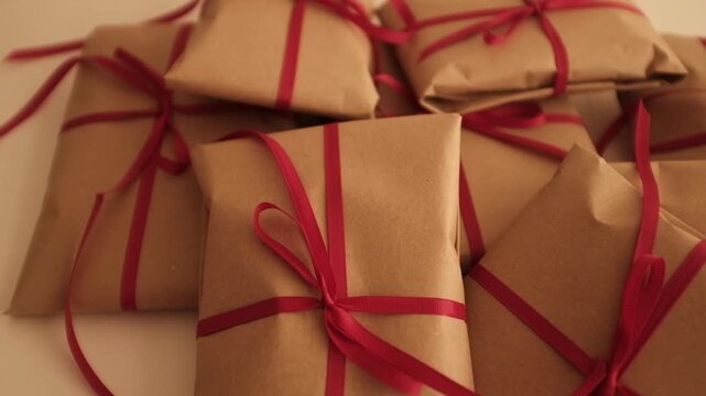 Christmas presents wrapped in brown craft paper and tied with thin red ribbon. Simple and modern wrapping aesthetics. Winter holidays gift giving tradition. Secret Santa.