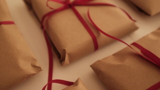 Christmas presents wrapped in brown craft paper and tied with thin red ribbon. Simple and modern wrapping aesthetics. Winter holidays gift giving tradition. Secret Santa.
