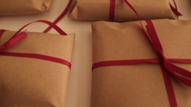 Christmas presents wrapped in brown craft paper and tied with thin red ribbon. Simple and modern wrapping aesthetics. Winter holidays gift giving tradition. Secret Santa.