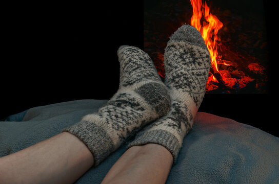 Winter scene with legs in gray woolen socks resting near glowing fireplace. Feelings of relaxation.