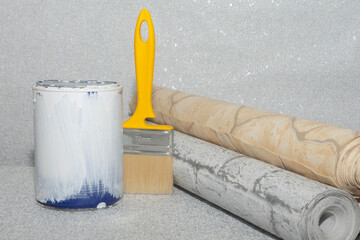 Textured wallpaper, a can of white paint, and a brush on a gray background. Concept for a home or apartment renovation