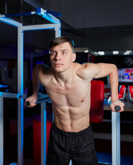 Muscular athlete performing parallel bar dips in a gym.