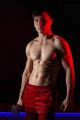 Young man posing with dumbbell in dramatic lighting