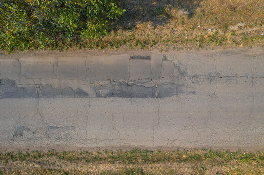 Cracked asphalt road surface with damaged patches and dry roadside grass