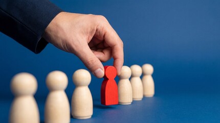 Recruitment decision concept with hand selecting red wooden figure from neutral candidates, talent identification, hiring choice, leadership strategy and workforce selection process.