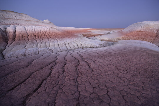 View of cracked earth and layered rock formations paint a surreal landscape under a tranquil sky, showcasing nature's artistry, Senek, Mangystau Region, Kazakhstan.