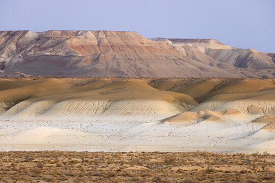 View of sun-baked earth tones cascading across undulating hills under a serene sky, painting a landscape of arid beauty, Senek, Mangystau Region, Kazakhstan.