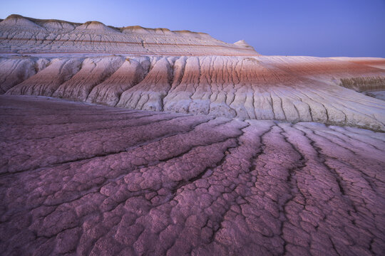 View of textured ground with warm colors meeting the cool tones of the rock formation under a twilight sky, Senek, Mangystau Region, Kazakhstan.