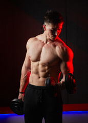 Muscular bodybuilder training biceps with dumbbells in red lighting.