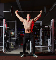 Muscular athlete performing standing overhead barbell press in a gym.