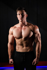 Portrait of a sweaty muscular bodybuilder posing on black background.