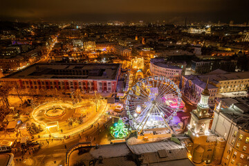 Aerial night view of a festive city with a Christmas market, ice rink, and Ferris wheel.