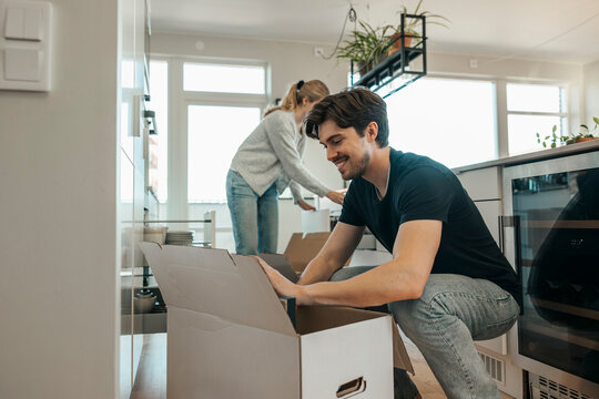 Smiling young man unpacking with girlfriend at new apartment