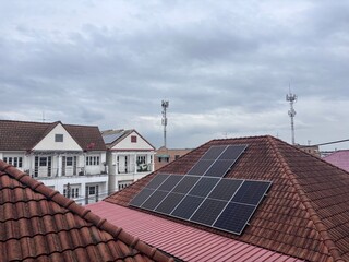 Solar panels installed on a residential brown tile roof in a suburban neighborhood under an overcast sky. This sustainable energy solution highlights renewable technology in urban housing development,