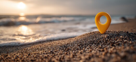 A vibrant yellow pin rests on a grainy beach. Ocean waves gently roll in during a golden sunset