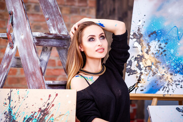 Beautiful young female artist in art studio surrounded by paintings