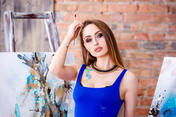 Beautiful young female artist in art studio surrounded by paintings