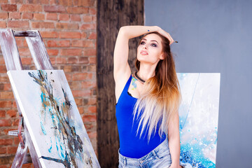 Beautiful young female artist in art studio surrounded by paintings