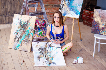 Beautiful young female artist in art studio surrounded by paintings