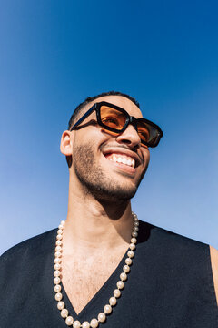 Low angle view of smiling young man with sunglasses looking away under blue sky
