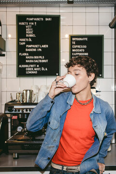 Short haired female barista drinking coffee while standing near counter in shop